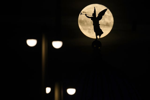 The full moon rises in the evening behind the angel "Fama" on the the Academy of Fine Arts, Tuesday, June 14, 2022, in Desden, Germany. (Robert Michael/dpa via AP)