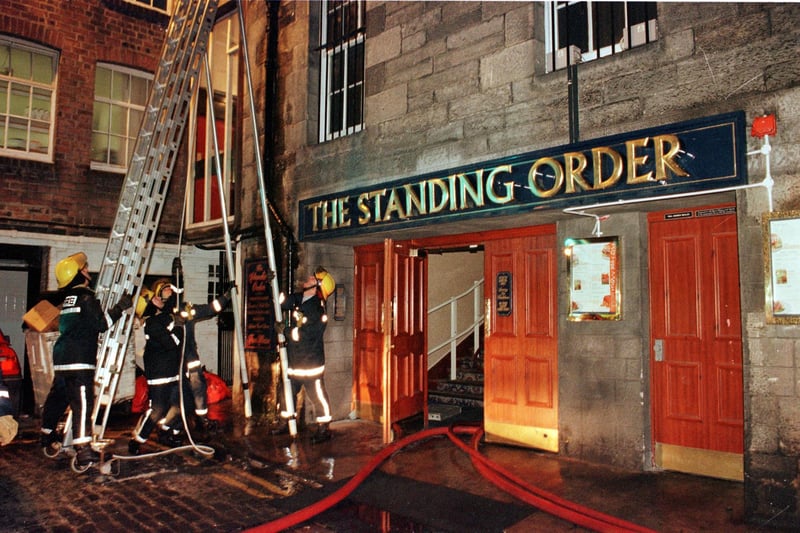 Firefighters erect ladders to tackle flames under the roof of the rear of the Standing Order pub in Rose Street North Lane, 20 February 2000.