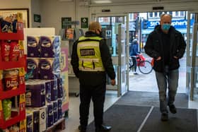 A security guard stands by the entrance to a Morrisons supermarket as a customer wearing a face mask enters the store. (Pic: Getty Images)