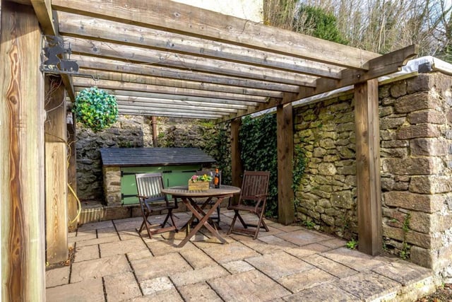 A patio at the side of the house has a pergola and woodstore.