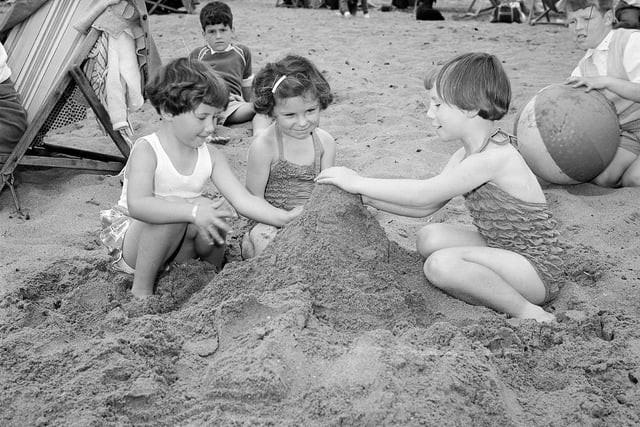 Three girls building a sandcastle on Cramond Beach in summer 1954.