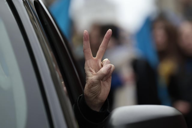 Someone gives the V sign gesture from a car as people take part in a march.