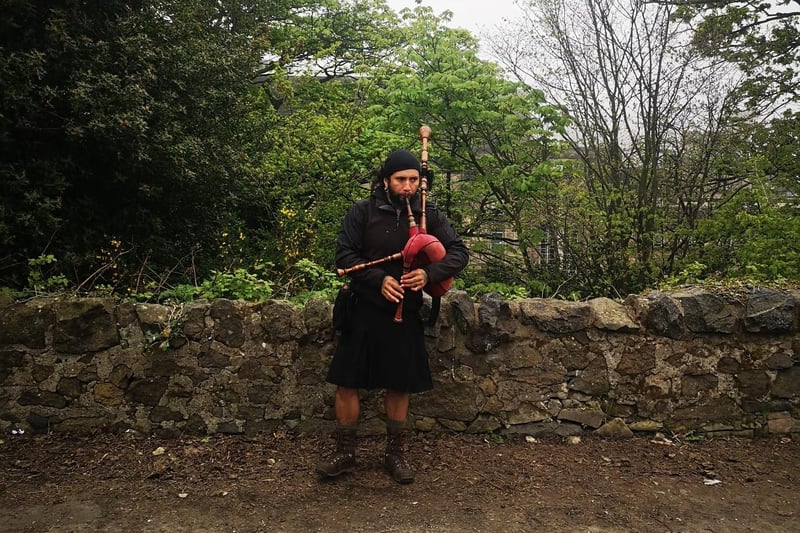 A piper plays the bagpipes while protesters gather on Calton Hill.