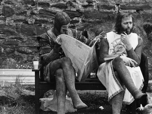 A chainmail-clad John Cleese reads a newspaper while Graham Chapman smokes a quiet pipe on the set of Monty Python and the Holy Grail (Picture: John Downing/Express/Getty Images)