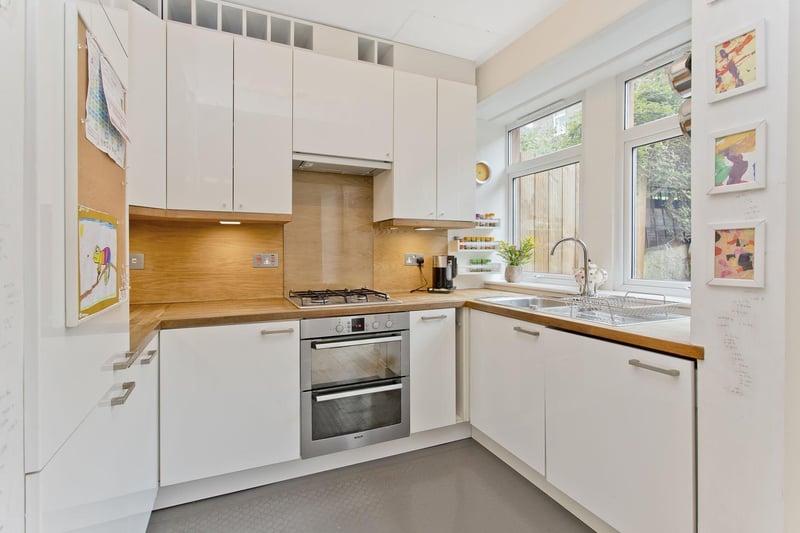 The kitchen is equipped with modern, gloss-white wall and base cabinets, solid oak worktops, and matching splashback panelling.