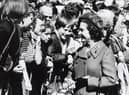 This picture shows the Queen smiling as she greets a crowd of people in Craigmillar and talking to some local children during her silver jubilee visit in 1977 .