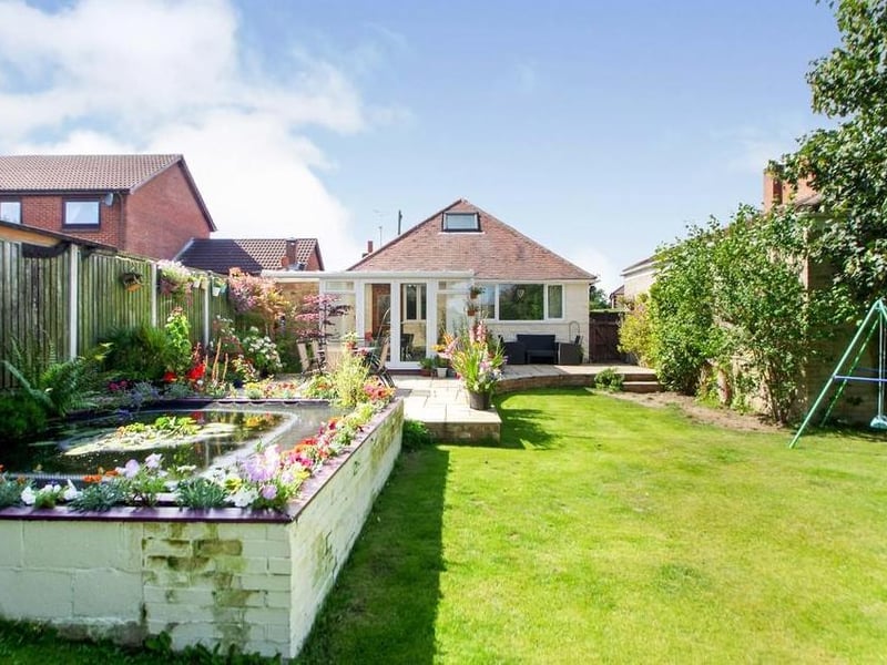 Another view of the private, landscaped back garden. The photo shows all its assets, including the fishpond, patio and manicured lawn.