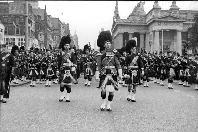 The Pipes and Drums of units performing at the Edinburgh Military Tattoo in 1964 march along Princes Street watched by a large crowd.