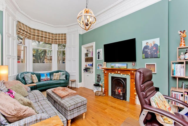 The living room is elegantly decorated and features beautifully detailed cornicing and a ceiling rose, a picture rail, handsome engineered wood flooring, and a homely fireplace flanked by an Edinburgh press with open shelving and hidden storage.
