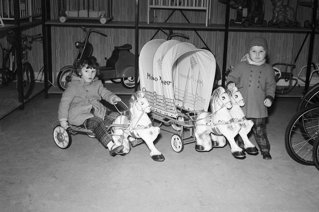 Two young children playing with a pony cart and a covered wagon in an Edinburgh toy shop.