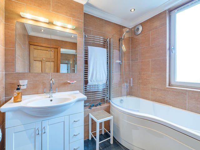 The family bathroom with white curved bath featuring a wall-mounted shower.