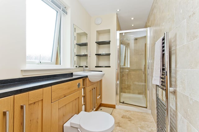 The bright en-suite shower room featuring a WC-suite, an enclosure with a rainfall shower, a towel radiator, and good vanity storage.