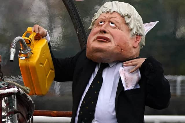 Performers from Ocean Rebellion dressed as Prime Minister Boris Johnson and an Oilhead set light to the sail of a small boat and they burn stacks of money on the banks of the River Clyde in Glasgow