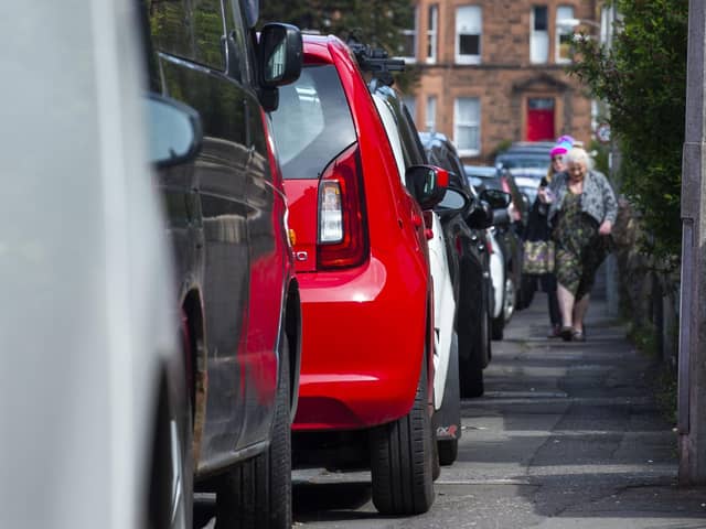 People struggle to pass cars parked on a narrow street pavement
