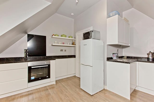 The other kitchen, on the second floor, with a fitted breakfast bar and space for a table and chairs. Both kitchens have a monochrome-inspired aesthetic with white handle-less cabinets and contrasting worktops.