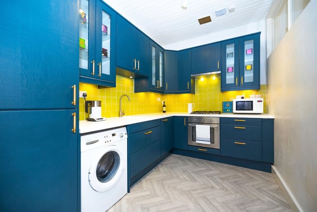 The kitchen has blue wall and floor units and is equipped with appliances such as a gas hob, extractor hood, oven and fridge/freezer.