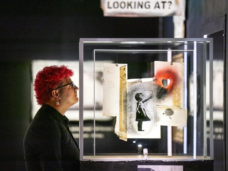 Gallery steward Louisa Mcgeachie takes a closer look the stencil piece of the girl with the heart balloon at the new show by artist Banksy 'Cut & Run' opens this Sunday at Glasgow's GoMA, revealing for the first time the stencils used to create many of the artist's most iconic works.