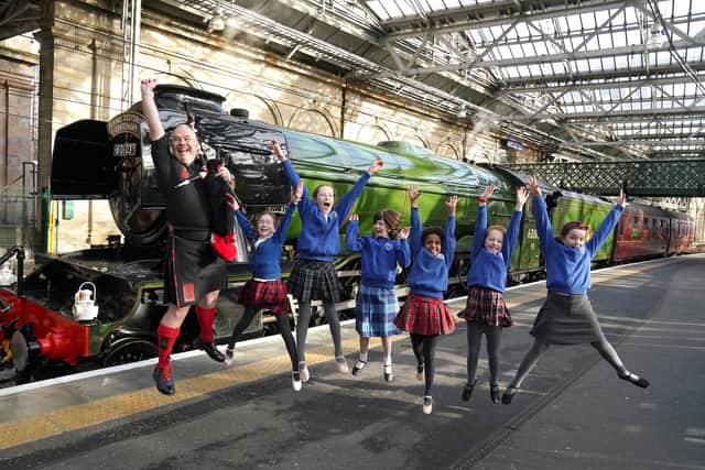 Piper Kevin MacDonald from the Red Hot Chilli Pipers with schoolchildren from Morningside Primary School and the Royal Scottish Country Dance Society beside Flying Scotsman at Edinburgh Waverley on Friday. Picture: Andrew Milligan/PA Wire