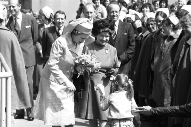 Queen Elizabeth II recieves a floral posy from a little girl as Prince Philip chats to nurses in the crowd in the background during a visit to Edinburgh Royal Infirmary in July 1979.