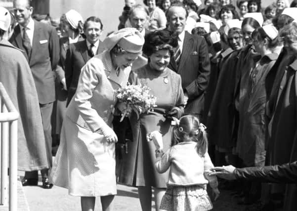 Queen Elizabeth II recieves a floral posy from a little girl as Prince Philip chats to nurses in the crowd in the background during a visit to Edinburgh Royal Infirmary in July 1979.