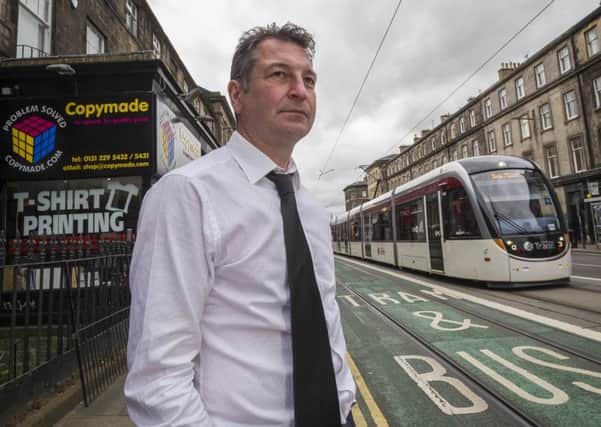 West End businessman Grant McKeeman of Copymade Ltd with trams passing outside his shop a year on from the line opening. Picture: Steven Scott Taylor