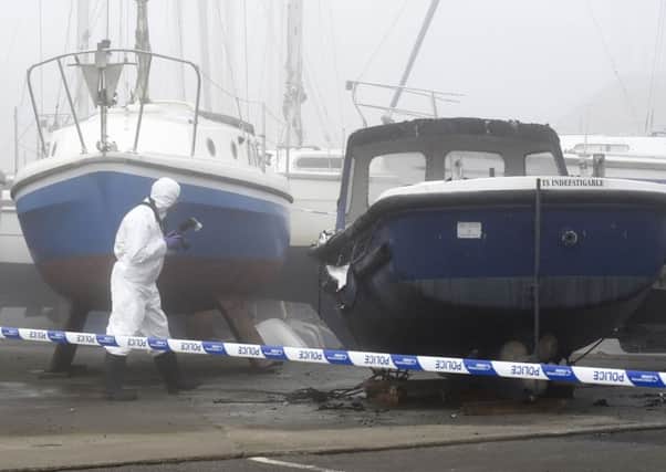 A police forensics officer investigates boats damaged by fire at Fisherrow Harbour. Picture: Jane Barlow
