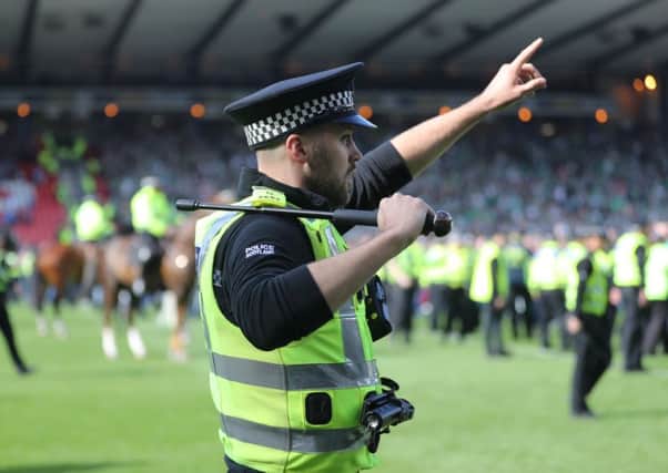 A policeman draws his baton as Hibs and Rangers fans invade the pitch at the final whistle after the Scottish Cup final. Picture: Getty
