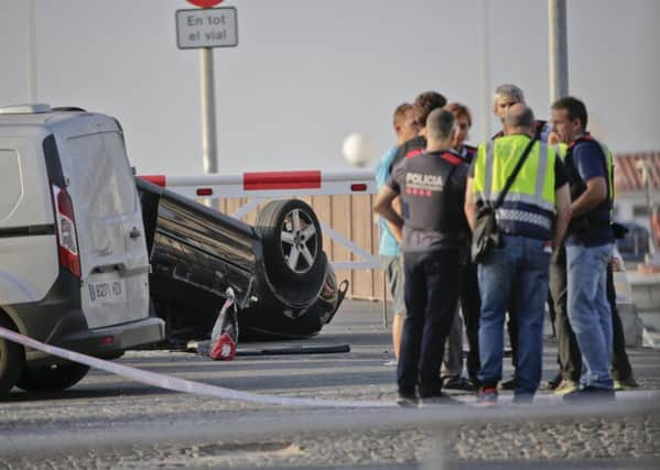 Police officers speak near an overturned car at the spot where terrorists were intercepted by police in Cambrils. Picture: AP