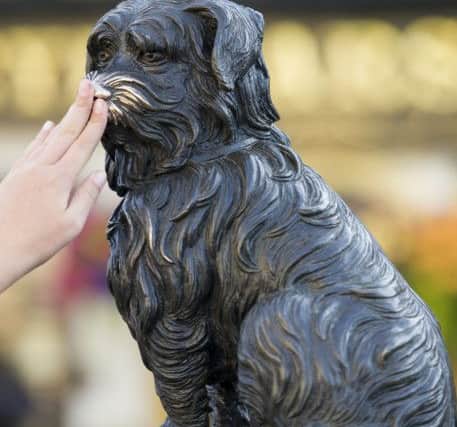 Tourists reach up to touch Greyfriars Bobby outside Greyfriars Kirk Edinburgh.