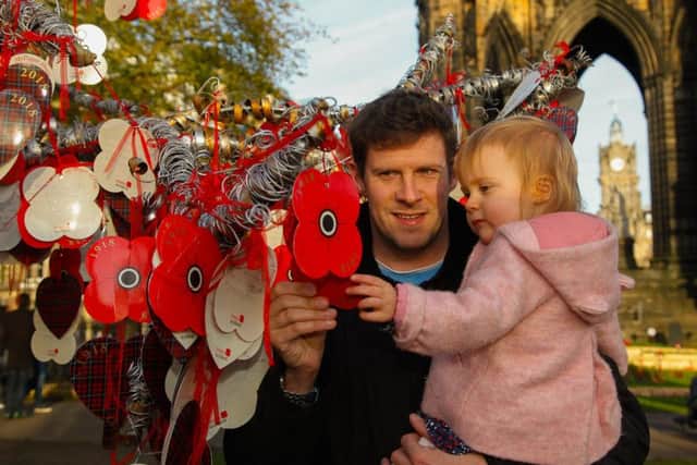 Princes St Gardens Garden Of Remembrance. Poppy Tree of Remembrance: Neil Cargill and his daughter Evelyn (22 mths) look for a note that Neil's mother put on the tree for Neil and for Neil's Great-Grandfather