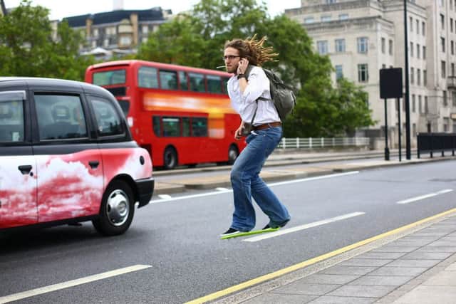 Man talking on the phone whilst riding a hoverboard across Waterloo Bridge as a black cab and bus drive by.