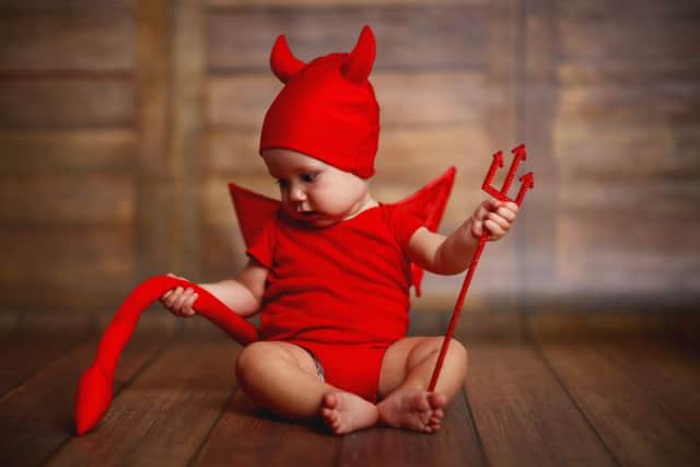 A baby in a devil halloween costume with horns and trident on a dark wooden background