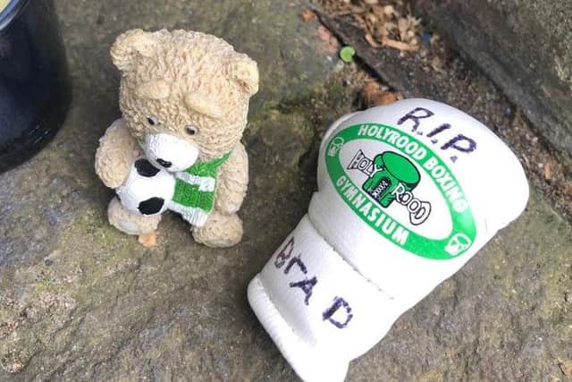 A teddy bear wearing a Hibs scarf and a green and white boxing glove with the message RIP Brad.